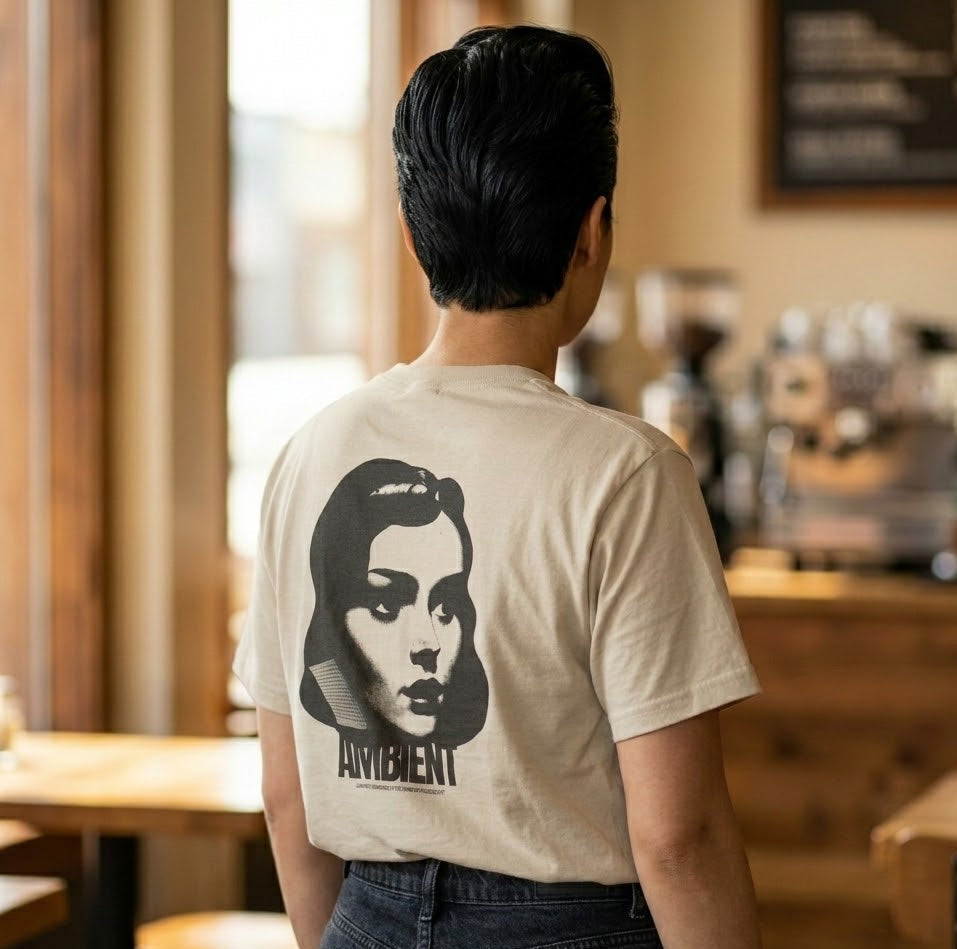 Person wearing a beige t-shirt with a graphic design in a coffee shop.